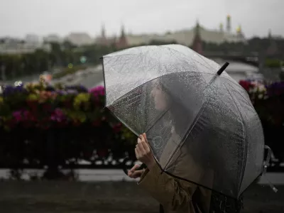 A woman crosses the Patriarshy footbridge holding a transparent umbrella on a rainy day in Moscow, Russia, Monday, June 30, 2025, with the Kremlin in the background. (AP Photo/Pavel Bednyakov)