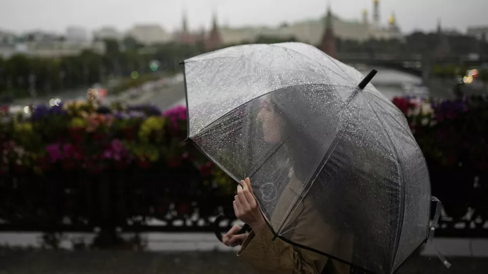 A woman crosses the Patriarshy footbridge holding a transparent umbrella on a rainy day in Moscow, Russia, Monday, June 30, 2025, with the Kremlin in the background. (AP Photo/Pavel Bednyakov)