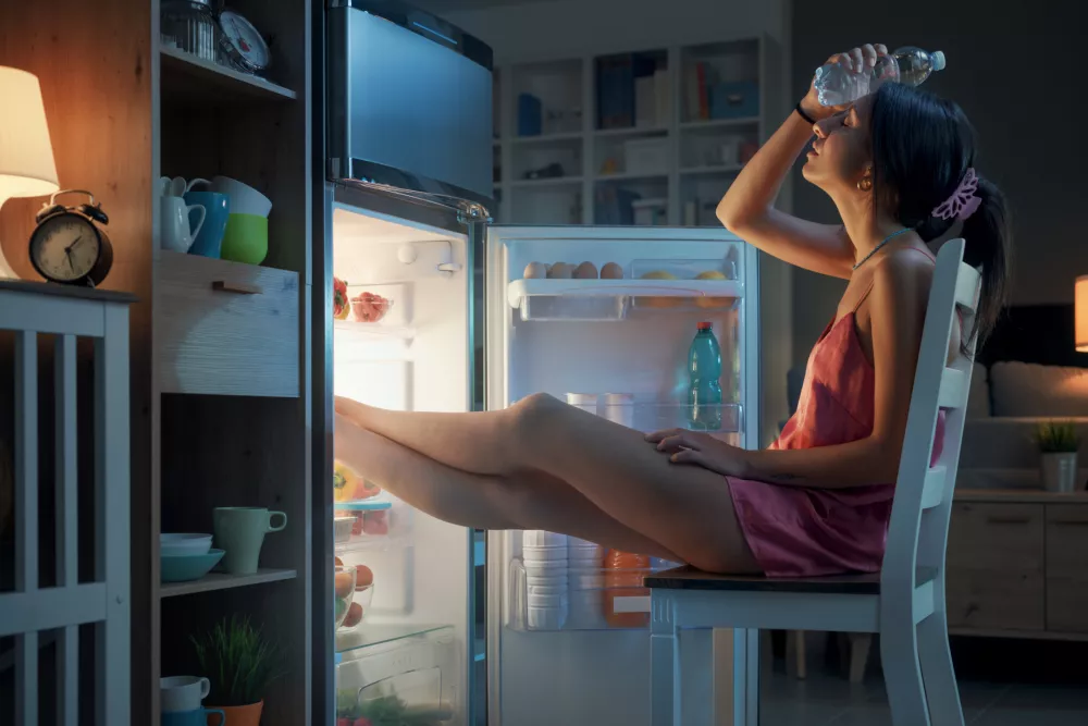 Woman suffering from the heat in summer, she is resting with her feet in the fridge and holding a water bottle / Foto: Demaerre