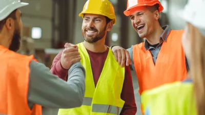 Attractive, happy, bearded, middle aged man wearing protective helmet shaking hands with colleagues standing in warehouse, greetings, deal. Concept of cooperation, communication / Foto: Mariia Vitkovska