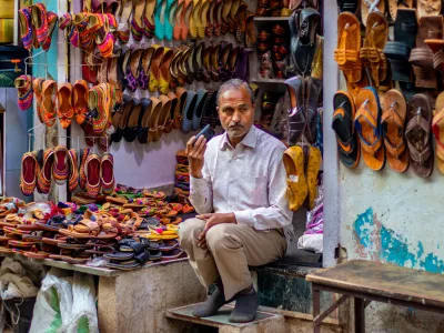 nathdwara, India – February 21, 2021: A shopkeeper sitting outside at his Juttis & Mojaris shop listening to something on the phone