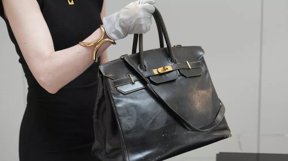 An auction officer carries the original Birkin bag created by Hermès for Jane Birkin in 1984, prior to its auction Thursday, July 10, 2025 in Paris. (AP Photo/Michel Euler)
