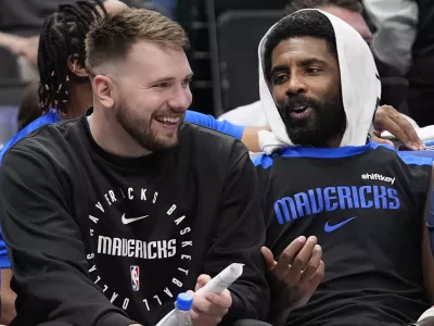 Sitting on the bench Dallas Mavericks guard Luka Doncic, left, shares a laugh with teammate fellow guard Kyrie Irving during a preseason NBA basketball game against the Milwaukee Bucks Thursday, Oct. 17, 2024, in Dallas. (AP Photo/LM Otero)