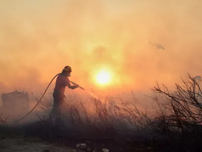 A firefighter tries to extinguish a wildfire as a helicopter flies, in the northwestern suburb of Kryoneri, in Athens, Greece, Saturday, July 26, 2025. (AP Photo/Yorgos Karahalis)