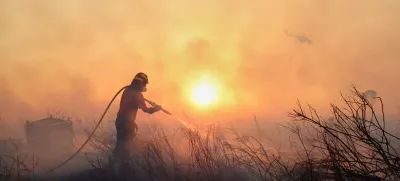 A firefighter tries to extinguish a wildfire as a helicopter flies, in the northwestern suburb of Kryoneri, in Athens, Greece, Saturday, July 26, 2025. (AP Photo/Yorgos Karahalis)