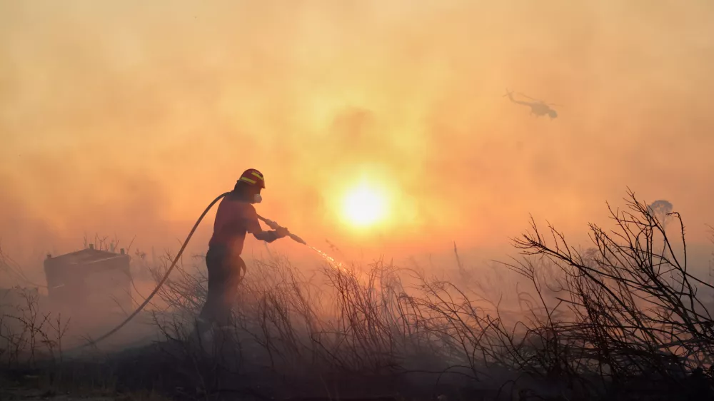 A firefighter tries to extinguish a wildfire as a helicopter flies, in the northwestern suburb of Kryoneri, in Athens, Greece, Saturday, July 26, 2025. (AP Photo/Yorgos Karahalis)