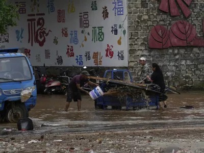 People clean their vehicle in floodwaters after heavy rain in Taishitun Town, Miyun district on the outskirts of Beijing, China, Monday, July 28, 2025. (AP Photo/Mahesh Kumar A.)