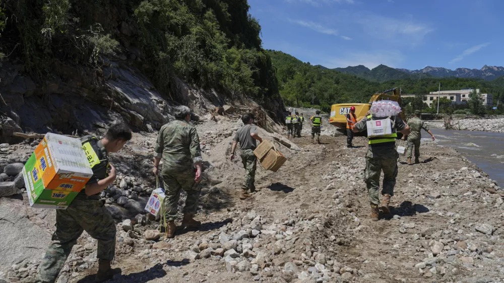 In this photo released by Xinhua News Agency, soldiers carry relief supplies for the trapped villagers by foot on a flood damaged road after heavy rains, in Miyun district on the outskirts of Beijing on Wednesday, July 30, 2025. (Ju Huanzong/Xinhua via AP)
