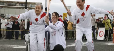 Torchbearer Shigeko Kagawa, left, hands over the flame of the torch to the next runner during a torch relay event for the Tokyo Olympics in Yamatokooriyama, Nara prefecture, western Japan, April 12, 2021. (Kyodo News via AP)