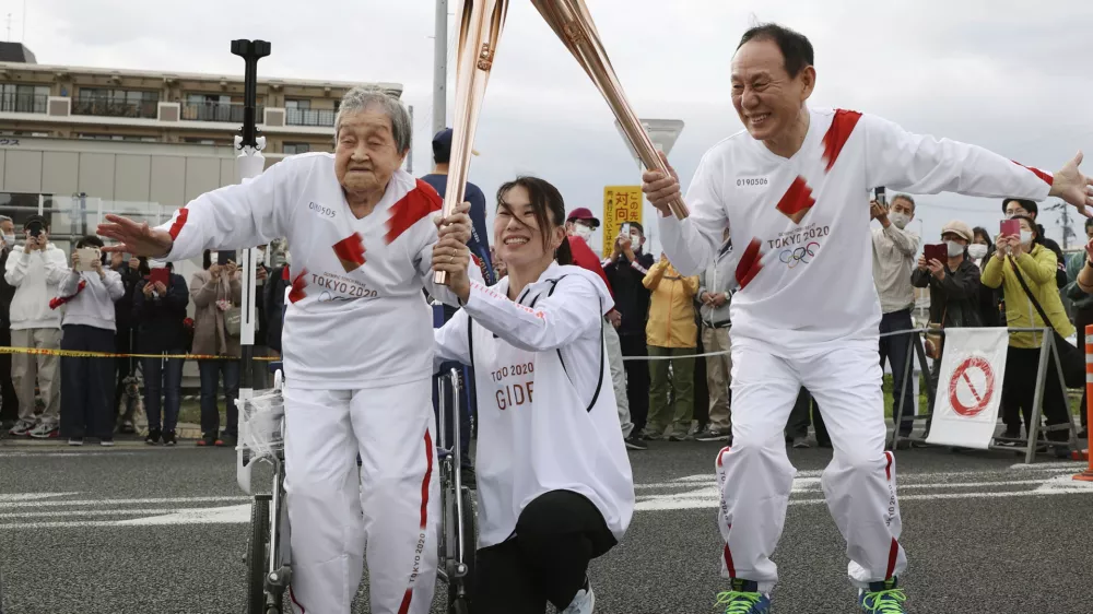 Torchbearer Shigeko Kagawa, left, hands over the flame of the torch to the next runner during a torch relay event for the Tokyo Olympics in Yamatokooriyama, Nara prefecture, western Japan, April 12, 2021. (Kyodo News via AP)