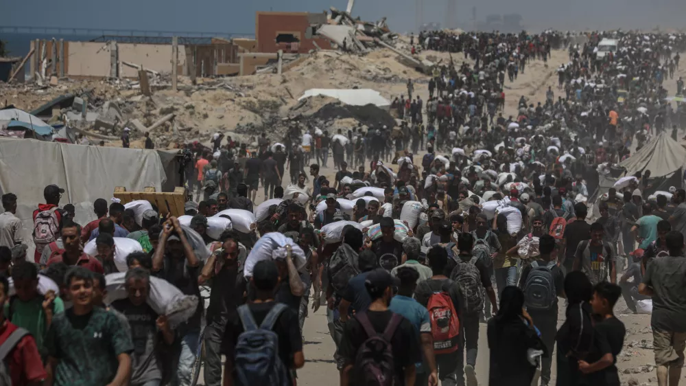 FILED - 01 August 2025, Palestinian Territories, Jabalia: Palestinians carry sacks of flour they collected from a humanitarian aid convoy, as they make their way along a destroyed road in Jabalia. Against the backdrop of a looming hunger crisis in the Gaza Strip, large-scale aid deliveries reached the besieged and embattled coastal area for the first time in months on Sunday. Photo: Omar Ashtawy/APA Images via ZUMA Press Wire/dpa