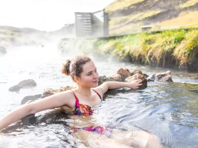 Young happy woman swimming bathing in Hveragerdi Hot Springs on trail in Reykjadalur, during autumn summer morning day in south Iceland, golden circle, rocks and river steam