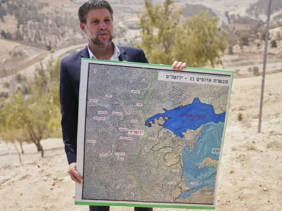 CORRECTS DAY Israeli Finance Minister Bezalel Smotrich holds a map that shows the E1 settlement project during a press conference near the settlement of Maale Adumim, in the Israeli-occupied West Bank, Thursday, Aug. 14, 2025. (AP Photo/Ohad Zwigenberg)