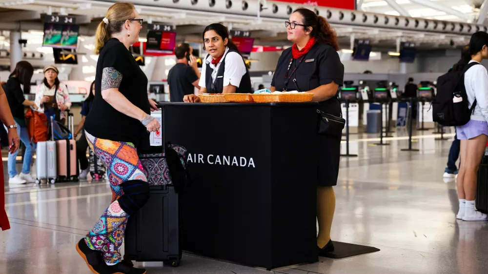 Air Canada workers speak with a passenger at a kiosk to deal with flight disruptions, ahead of a potential strike by flight attendants of the airline, at the Toronto Pearson International Airport in Mississauga, Ontario, Canada, August 15, 2025. REUTERS/Cole Burston