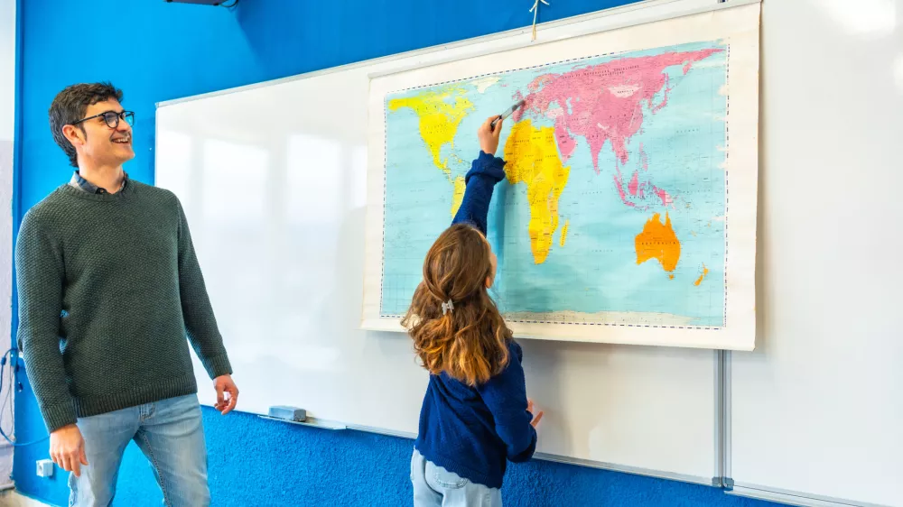 Girl pointing at world map during geography lesson with her teacher in elementary school classroom / Foto: Unaihuiziphotography