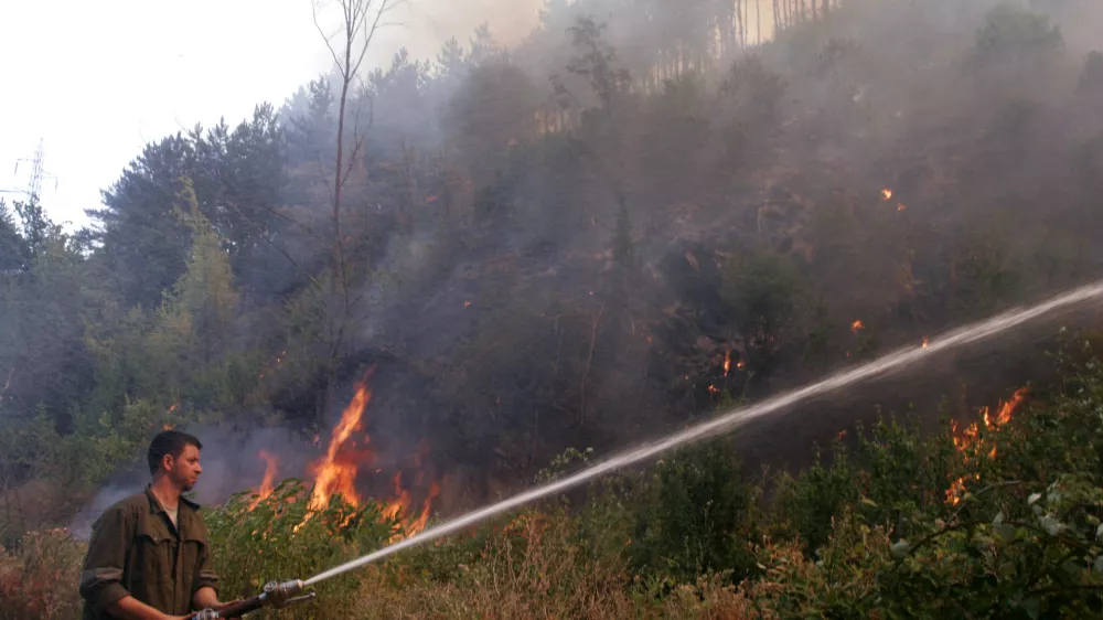 A fire fighter sprays water over a forest fire near the village of Dubovo, some 240 km (150 miles) east of Sofia, July 27, 2007. A heatwave that has roasted much of the Balkans for a week abated in the north on Wednesday but sizzled on in Greece and left scores of wildfires throughout the region. REUTERS/ Nikolay Doychinov (BULGARIA)