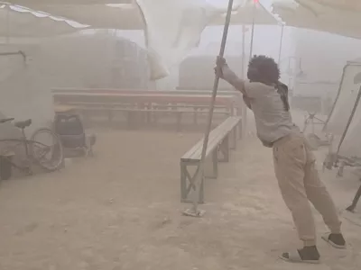 A man holds up a tent structure amid a dust storm near Burning Man festival's Black Rock Desert site, a day before the annual festival's start, in Gerlach, Nevada, U.S., August 23, 2025, in this still image obtained from a social media video. Simba Khela/via REUTERS THIS IMAGE HAS BEEN SUPPLIED BY A THIRD PARTY. NO RESALES. NO ARCHIVES. MANDATORY CREDIT. VERIFICATION: Reuters was able to confirm the location of the video from corroborating footage posted on social media. Date of footage was confirmed on file data. National Weather Service (NWS) said in a statement that there was dust storm 9 miles northwest of Lovelock 23 August (Saturday). Burning Man event starts on August 24 in Black Rock Desert.