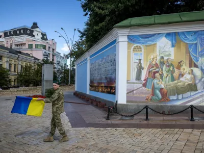 A soldier carries a Ukrainian national flag outside St. Michael's Golden-Domed Monastery, amid Russia's attack on Ukraine, in Kyiv, Ukraine August 25, 2025. REUTERS/Thomas Peter