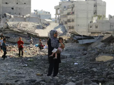 A Palestinian woman carries a child, as they inspect the site of an overnight Israeli strike on a house, in Gaza City, August 26, 2025. REUTERS/Ebrahim Hajjaj