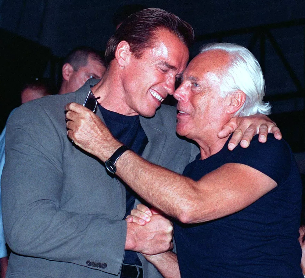 FILE - Actor Arnold Schwarzenegger hugs Italian fashion designer Giorgio Armani at the end of Emporio Armani's Spring-Summer 1999 Men's collection Fashion Show in Milan, June 29 1998. (AP Photo/Antonio Calanni, file)