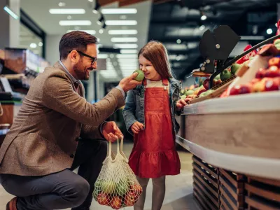 Father and daughter smiling apple, tasting quality while buying groceries in market