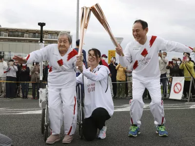 Torchbearer Shigeko Kagawa, left, hands over the flame of the torch to the next runner during a torch relay event for the Tokyo Olympics in Yamatokooriyama, Nara prefecture, western Japan, April 12, 2021. (Kyodo News via AP)