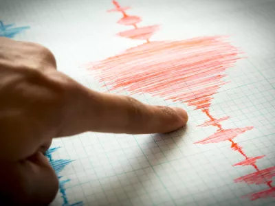 Seismological device for measuring earthquakes. Seismological activity lines on the sheet of measuring paper. Earthquake wave on graph paper. Vignette image. Human finger showing a detail.