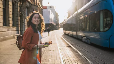 Woman with phone and sunglasses walking across city street next to blue tram. Concept: urban lifestyle, travel experience, exploring Croatia.