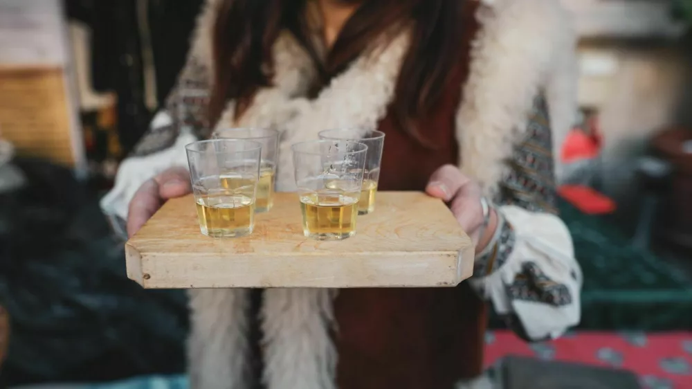 Shallow depth of field (selective focus) image with a woman holding a wooden plate with palinca (or tuica), romanian traditional plum brandy.
