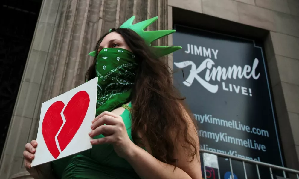 A woman wears a Statue of Liberty costume as she holds an image of a broken heart, outside the El Capitan Entertainment Centre, where "Jimmy Kimmel Live!" is recorded for broadcast, on Hollywood Boulevard in Los Angeles, California, U.S. September 17, 2025. REUTERS/Daniel Cole   TPX IMAGES OF THE DAY