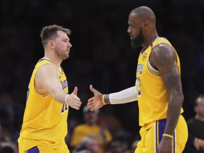 Los Angeles Lakers guard Luka Doncic, left, touches hands with teammate forward LeBron James during the first half of an NBA basketball game against the Utah Jazz, Monday, Feb. 10, 2025, in Los Angeles. (AP Photo/Mark J. Terrill)