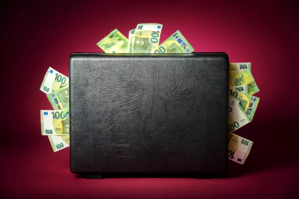 A briefcase overflowing with euro banknotes. Concept studio shot on illuminated burgundy red background with dark vignette / Foto: Smileus