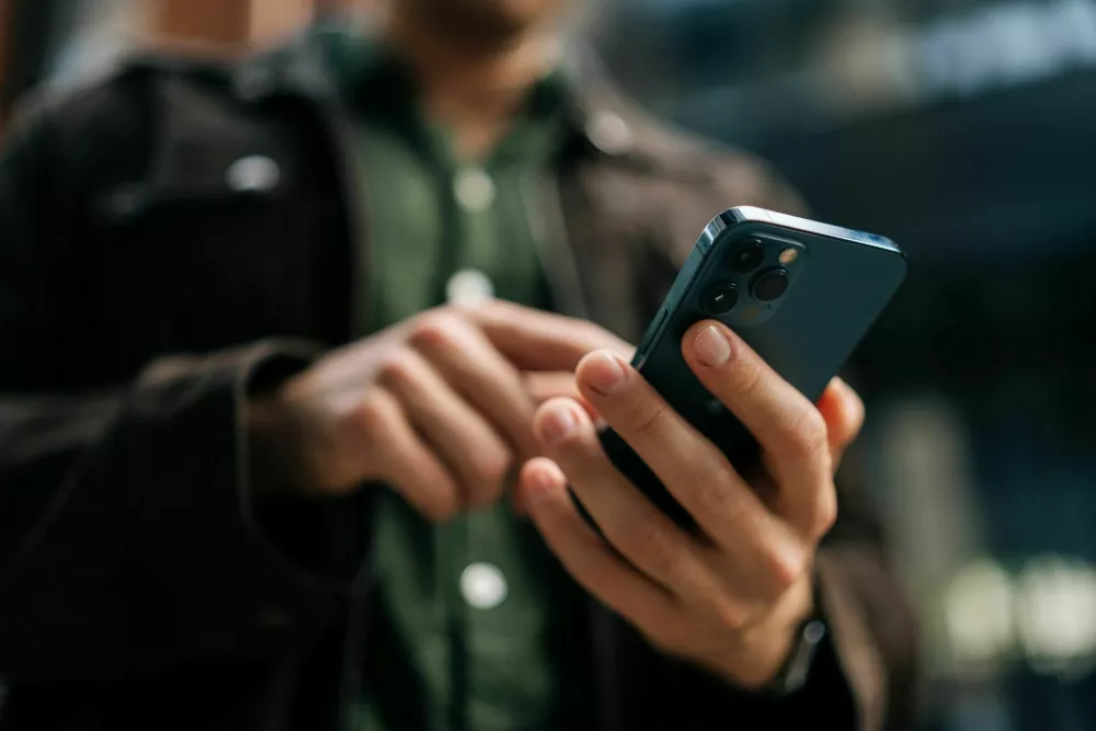 Close-up hands of unrecognizable man holding and using smartphone standing on city street, browsing internet, checking social media, using mobile application. Concept of modern communication.