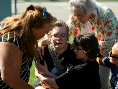 Joanne Green of Fenton, 75, top right, and McKenna Harrington of Davison, 25, second from right, comfort Katelyn Kruse of Fenton, 26, center, after Kruse was present at the scene of a shooting and structure fire at The Church of Jesus Christ of Latter-day Saints on McCandlish Road in Grand Blanc, Mich., Sunday, Sept. 28, 2025. (Katy Kildee/Detroit News via AP)