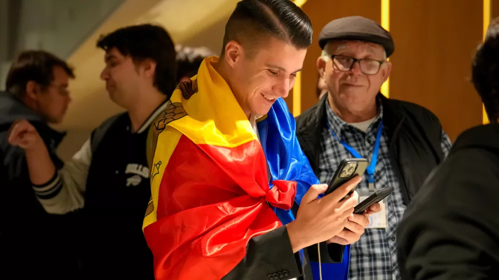 A supporter of the pro-EU Party of Action and Solidarity (PAS) draped in the Moldovan flag smiles as he checks partial results on a phone after the polls closed for the parliamentary election, in Chisinau, Moldova, Sunday, Sept. 28, 2025. (AP Photo/Vadim Ghirda)