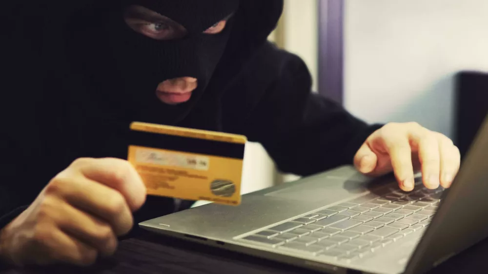 W2M8KX Man in robber mask and hood misappropriates personal bank data. Cyber fraudster attacks online banking system. Hacker makes financial fraud via