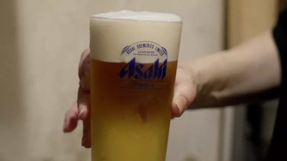 A staff of a restaurant Kushiyaki Tosaka holds a freshly poured glass of Asahi Super Dry beer at the restaurant in Tokyo, Japan, October 3, 2025. REUTERS/Joseph Campbell