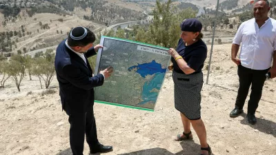 Israeli Finance Minister Bezalel Smotrich and a woman hold a map that shows the long-frozen E1 settlement scheme, that would split East Jerusalem from the occupied West Bank, on the day of a press conference near the Israeli settlement of Maale Adumim, in the Israeli-occupied West Bank, August 14, 2025. REUTERS/Ronen Zvulun