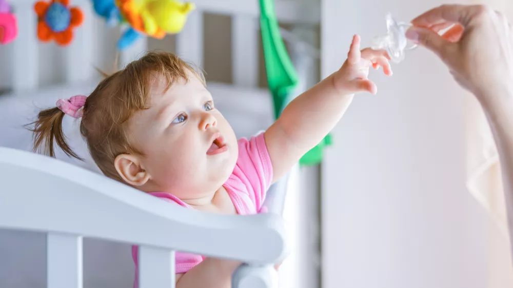 ﻿Little girl pulls her hand to the dummy, standing in a baby crib