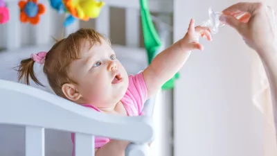 ﻿Little girl pulls her hand to the dummy, standing in a baby crib