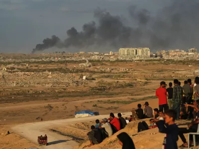 Displaced Palestinians watch smoke rise after Israeli military strikes as they gather on the coastal road near Wadi Gaza, in the central Gaza Strip, Thursday, Oct. 9, 2025. (AP Photo/Abdel Kareem Hana)