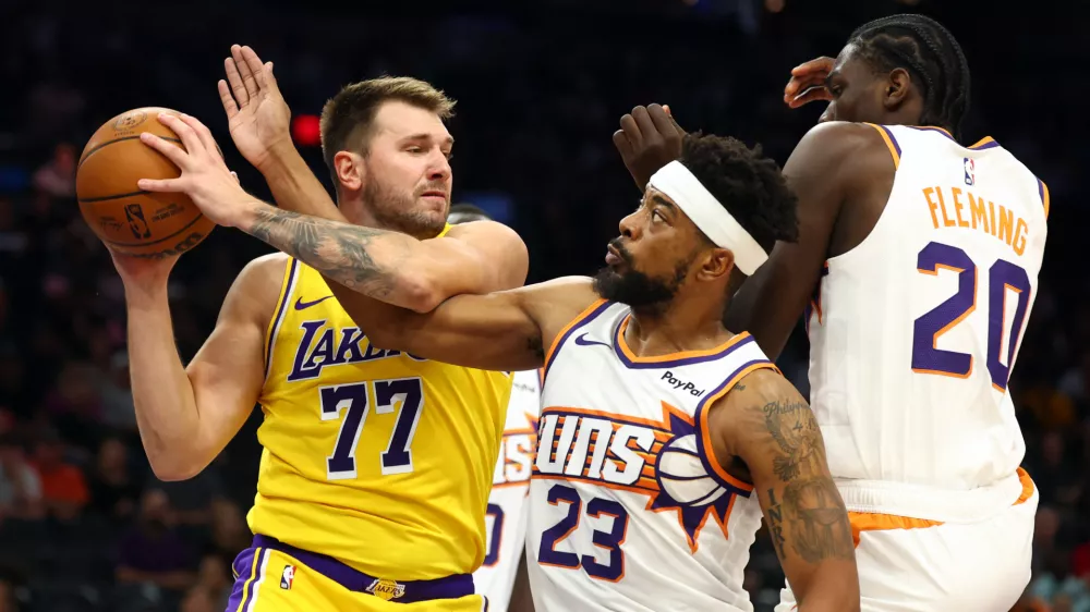 Oct 14, 2025; Phoenix, Arizona, USA; Los Angeles Lakers guard Luka Doncic (77) grabs a rebound against Phoenix Suns guard Jordan Goodwin (23) and forward Rasheer Fleming (20) during an NBA preseason game at Mortgage Matchup Center. Mandatory Credit: Mark J. Rebilas-Imagn Images