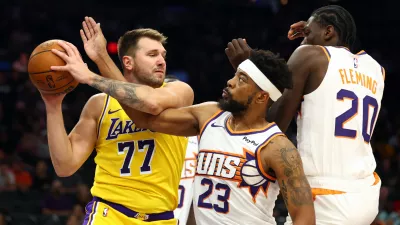 Oct 14, 2025; Phoenix, Arizona, USA; Los Angeles Lakers guard Luka Doncic (77) grabs a rebound against Phoenix Suns guard Jordan Goodwin (23) and forward Rasheer Fleming (20) during an NBA preseason game at Mortgage Matchup Center. Mandatory Credit: Mark J. Rebilas-Imagn Images