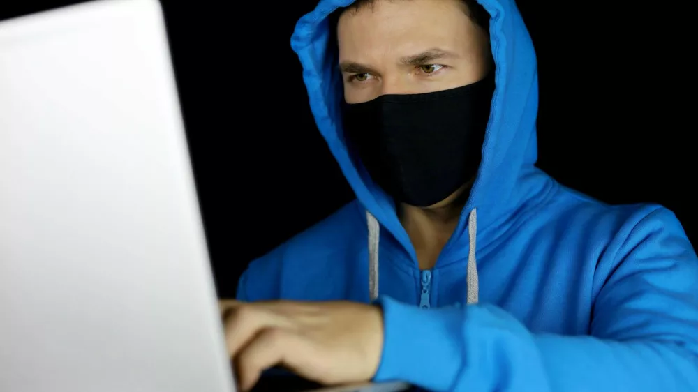 Moški za računalnikom z masko na obrazu