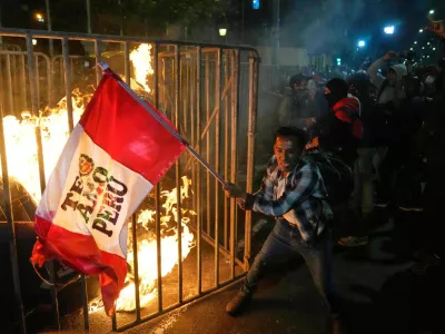 A demonstrator waves a Peruvian flag as a cardboard doll burns in front of Congress during a protest against the newly installed President Jose Jeri in Lima, Peru, Oct. 15, 2025. (AP Photo/Martin Mejia)