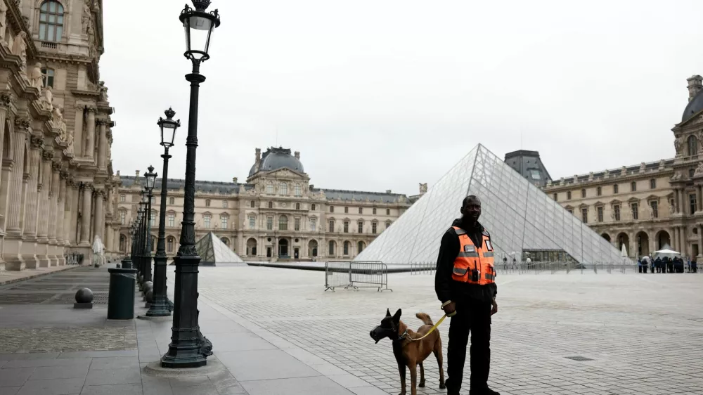 A security employee with a dog stands near the glass Pyramid of the Louvre Museum as the museum remains closed the day after a spectacular jewel heist by thieves who broke into the landmark by using a crane and smashing an upstairs window, stealing priceless jewelry from an area that houses the French crown jewels before escaping on motorbikes, in Paris, France, October 20, 2025. REUTERS/Benoit Tessier