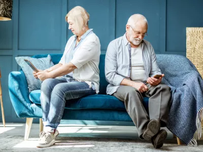 Offended senior man and woman sitting back to each other, using digital gadgets on the couch at home / Foto: Rosshelen