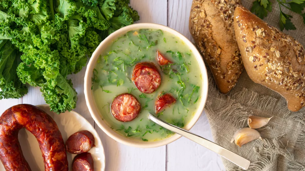 Portuguese style soup called Caldo Verde, bread, Cabbage julienne, and chorizo sausage on a white wooden Table. Flat lay / Foto: Iggi_boo