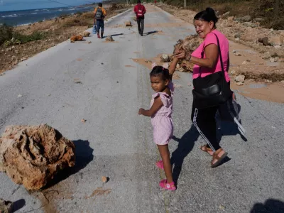 People pass by rocks washed onto a road by Hurricane Melissa on the southern coast of Santiago de Cuba, Thursday, Oct. 30, 2025. (AP Photo/Ramon Espinosa)