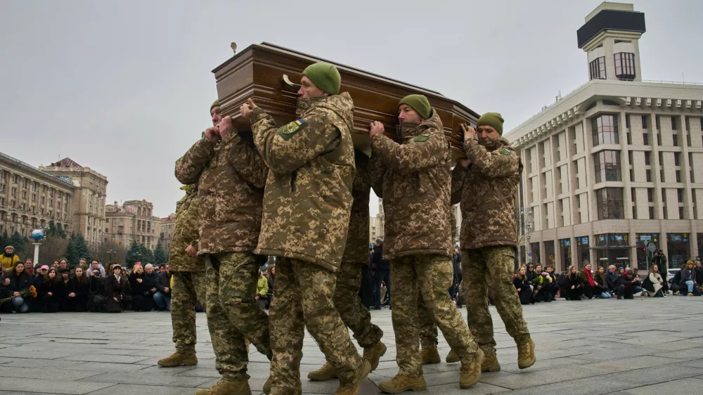 People kneel down as Ukrainian servicemen carry the coffin of their fellow-soldier and a well-known documentary photographer Kostiantyn Huzenko, 28, who was killed in Russia-Ukraine war, during the funeral ceremony in the Independence square in Kyiv, Ukraine, Friday, Nov. 7, 2025. (AP Photo/Efrem Lukatsky)